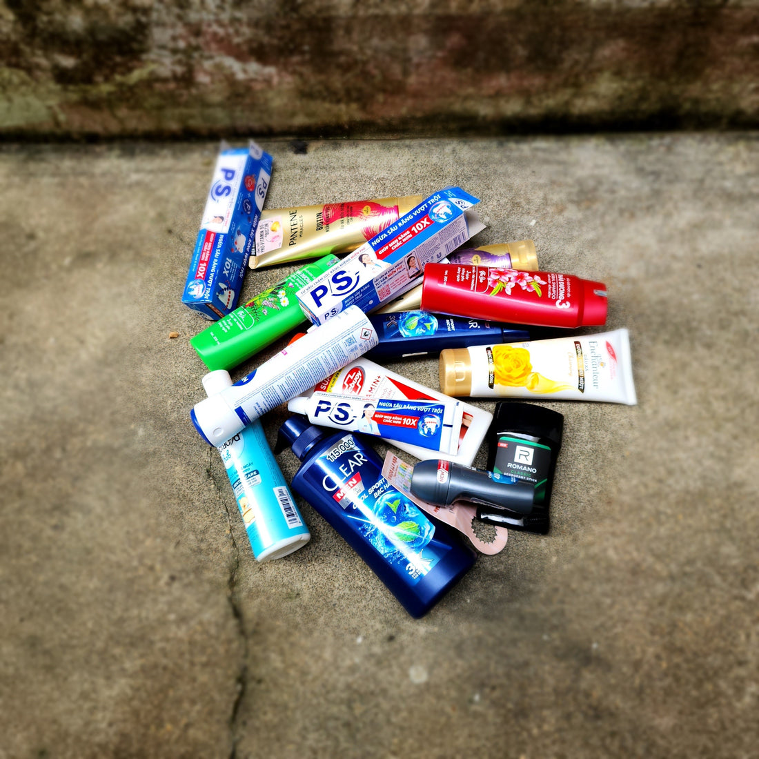 Discarded plastic and laminated cardboard personal care packaging piled on pavement — the kind of conventional tube and carton waste that doesn't break down or get recycled cleanly.