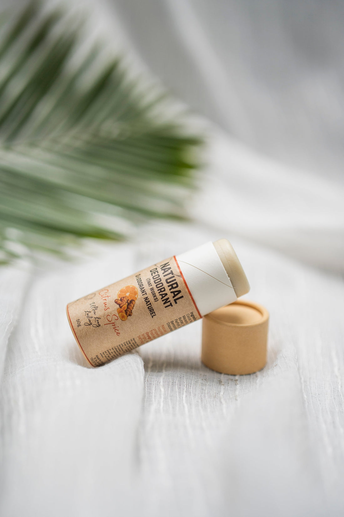 Natural deodorant stick with citrus spice scent, eco-friendly packaging on white fabric with palm leaf