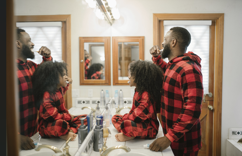 father and daughter brushing their teeth together in red plaid pajamas