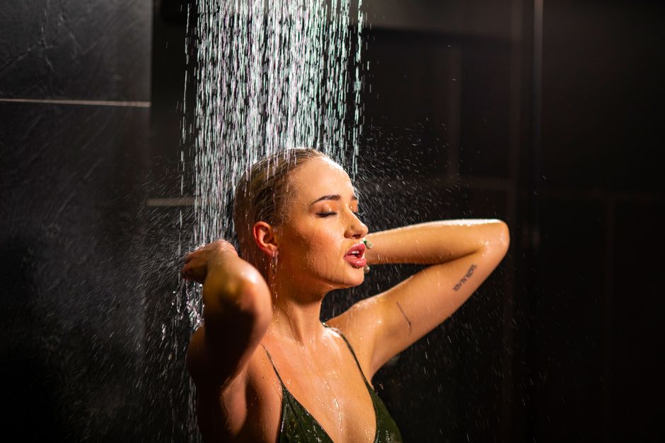 A woman enjoys a rejuvenating shower with water pouring over her, embracing a moment of relaxation.