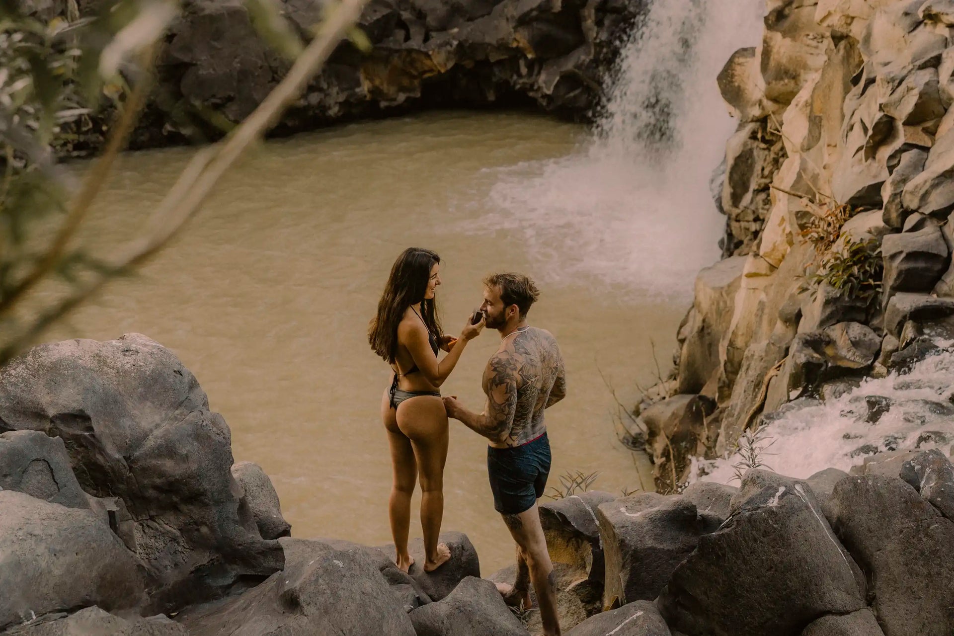Couple applying natural deodorant by waterfall, enjoying outdoor adventure with clean, sustainable body care.