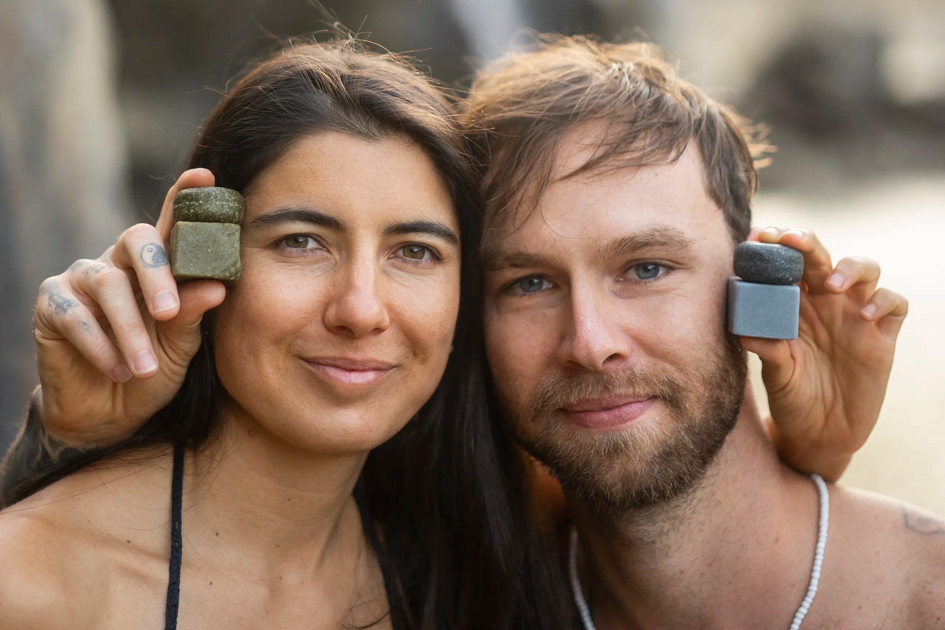 Couple holding natural soap bars, smiling outdoors — clean, simple, sustainable skincare for adventures
